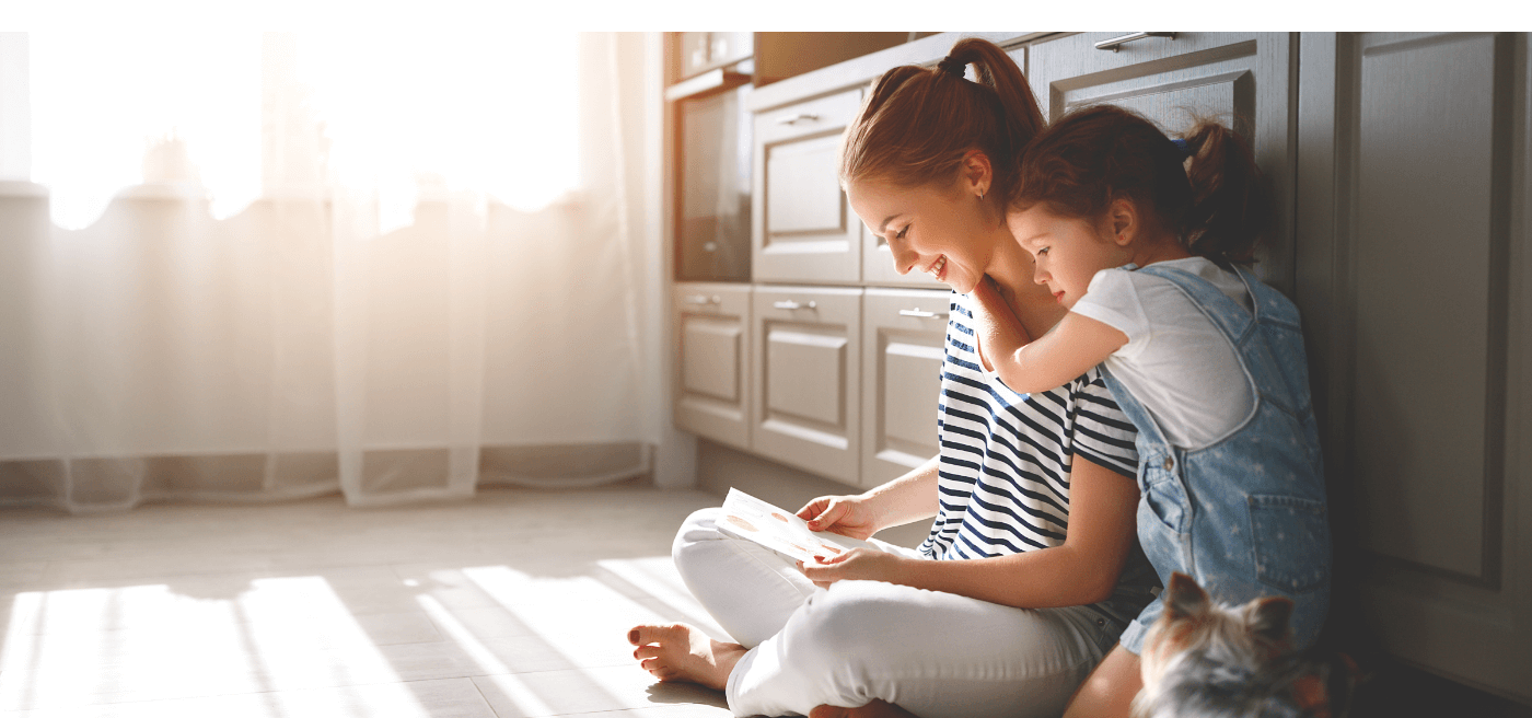 Mother and daughter sitting on floor of kitchen while reading