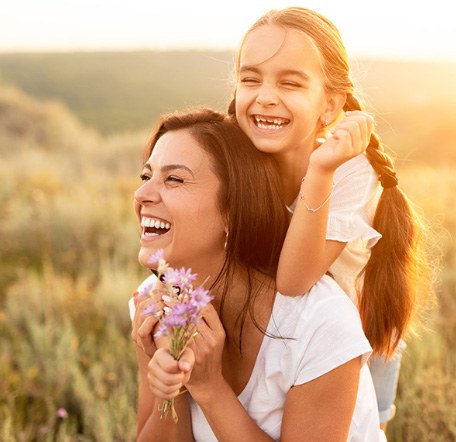 Laughing mother and daughter laughing outdoors with flowers