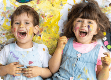 Two kids laying on floor covered in paint spots