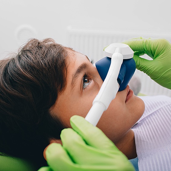 Green-gloved hands placing nitrous oxide mask over little boy’s nose