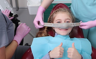 Little girl giving two thumbs up as nitrous oxide mask is removed