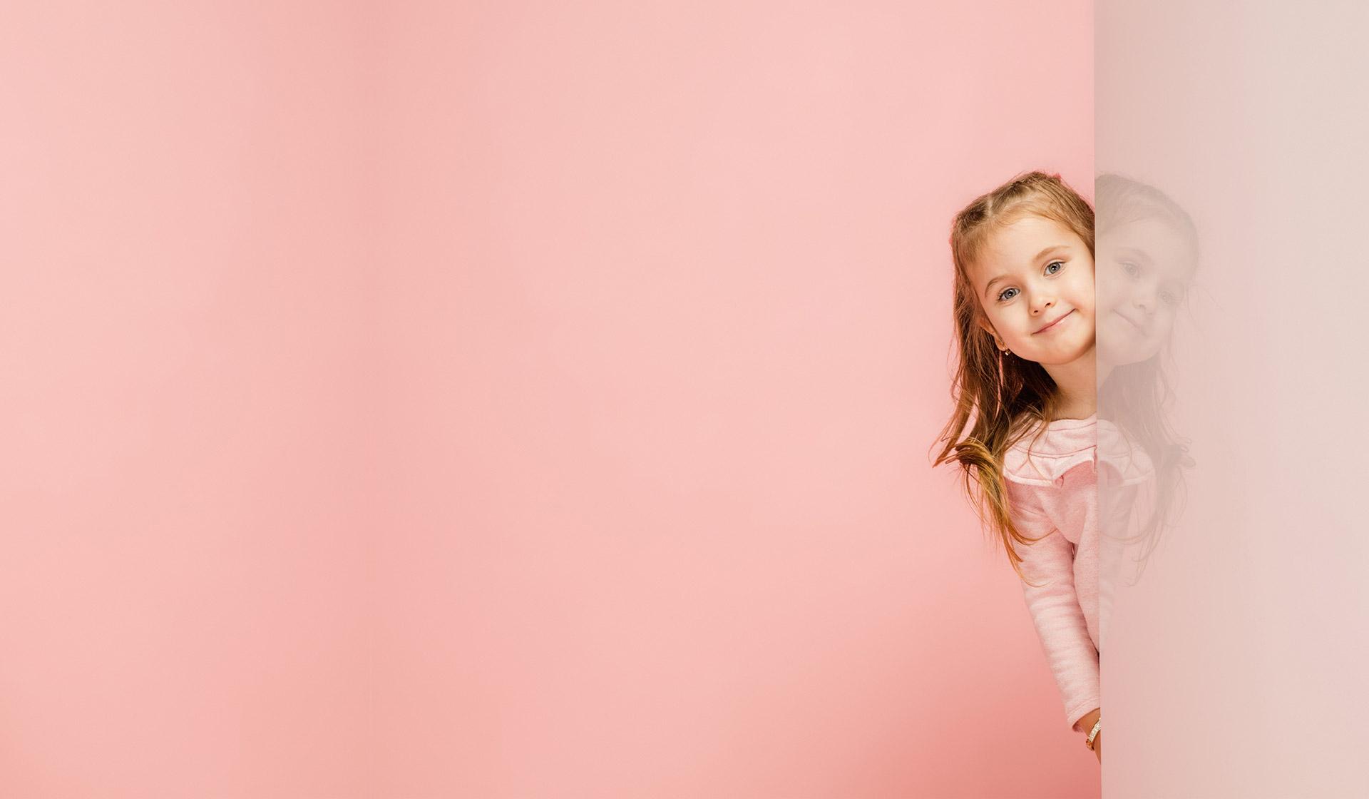 Young girl peeking from behind pink wall with pink background