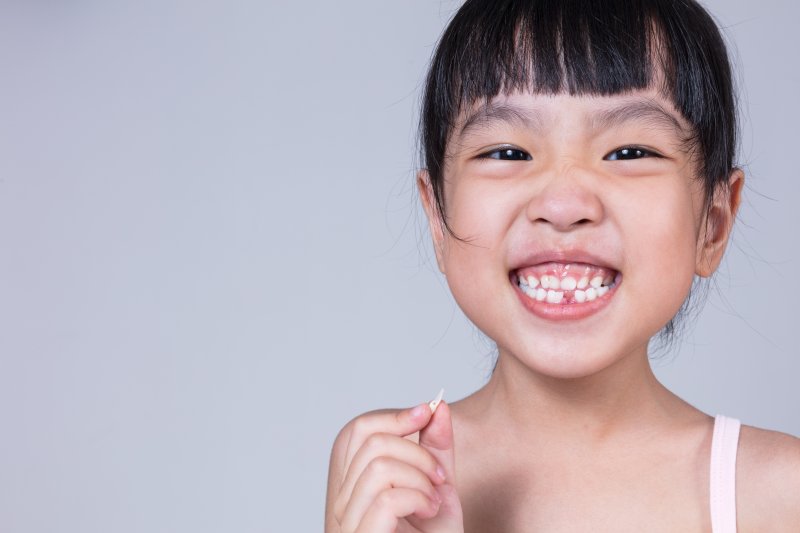 A child smiling and holding their tooth after a tooth extraction