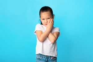 Girl holding both hands to jaw in pain with blue background